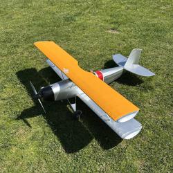 Model biplane on grass, with bright orange upper wing and silver body.