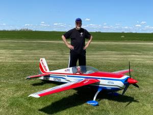 Man standing on grass beside a large radio-controlled model airplane.