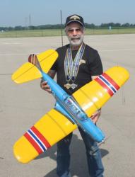 Man smiling, holding a large yellow and blue model airplane, wearing medals.
