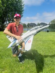 Teen wearing a red cap kneeling on grass, holding a model jet plane with blue stripes.