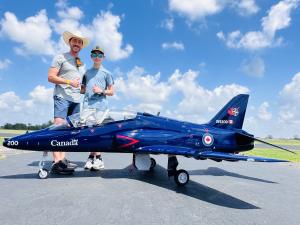 Father and son pose with small blue model jet on runway.