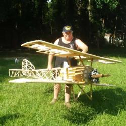 Man holding a large model biplane on grass.