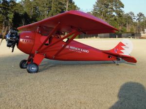 Red vintage airplane on grassy field with trees in the background.
