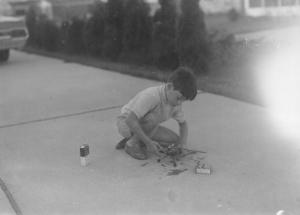 Child playing with toy cars on a driveway.