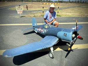 Man kneeling beside a large blue model aircraft on an airstrip.
