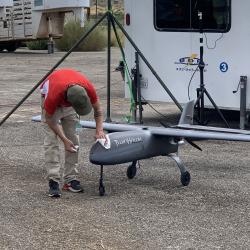 Man cleans a small gray drone parked outside.