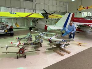 Man arranging model airplanes in a hangar with vintage aircraft displays.