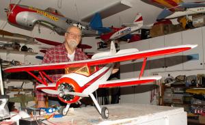 Man with model biplane in a hobby workshop.