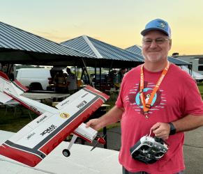 Man holding remote control airplane, smiling at outdoor event.