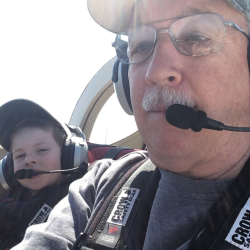 Father and son in cockpit, wearing headsets and seatbelts.
