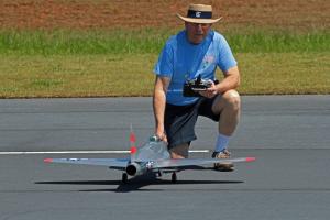 Man kneeling on runway with model airplane, holding remote control.