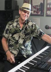 Man in floral shirt and hat playing keyboard, smiling.