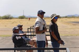 Two young men, wearing hats and sunglasses, stand outdoors with remote controllers.