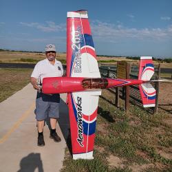 Man standing with large red and white model airplane outdoors.
