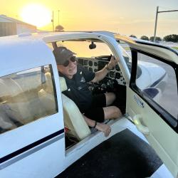 Man smiling in small airplane cockpit at sunset.
