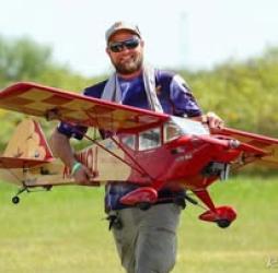 Man carrying large red model plane outdoors.