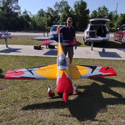 A man standing behind a large red and yellow RC plane on grass.