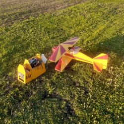 A small, colorful model airplane on grass near equipment in sunlight.