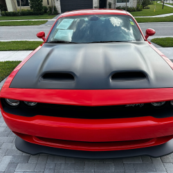 Red sports car with a matte black hood parked on a paved driveway.
