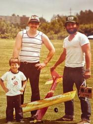 Two men and a boy with a model airplane on grass.