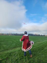 Person in a Santa coat flying a small plane in a green field.