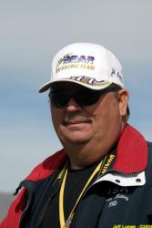 Man in sunglasses and racing cap, wearing a red and blue coat.