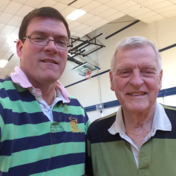 Two men smiling in a gym, wearing striped shirts.