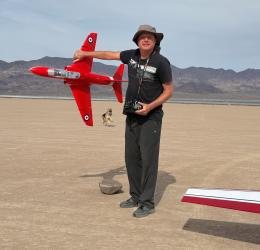 Man holding a red model jet in a desert landscape.