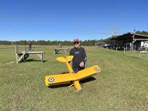 Man with large yellow model plane on grassy field.