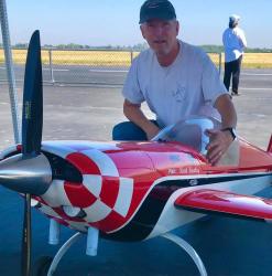 Red and white model plane on airstrip with man kneeling beside it.