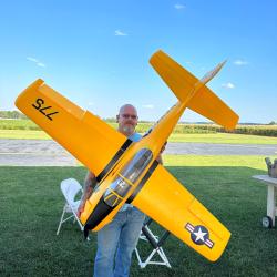 Man holding large yellow model airplane outdoors on a sunny day.