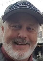 Smiling man with a beard and cap, outdoors.