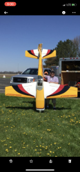 Large yellow model airplane on grass, parked near a truck.