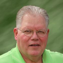 Older man with glasses, wearing a green shirt, against a blurred green background.