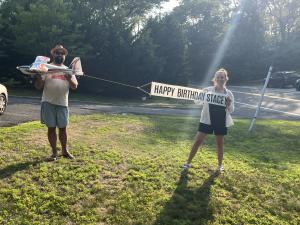 Man and woman outdoors with toy airplane and "Happy Birthday Stacey" banner.