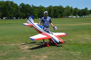 A person holding a large model airplane on a grassy field.