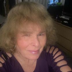 Older woman smiling, wearing a purple top, inside a room.