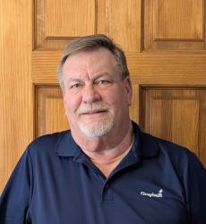 Man in a navy polo shirt smiling, standing in front of a wooden door.