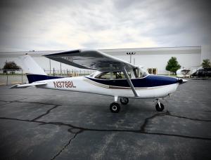 Small white and blue propeller plane on tarmac, hangar in background.