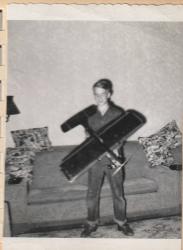 Black and white photo of a boy smiling, holding a model airplane in a living room.
