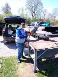 Man smiling and standing outside by a table with an open car trunk in the background.