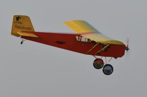 Red and yellow model airplane with large wheels in flight.