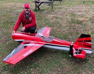 Man kneeling next to a large red and white model airplane on grass.