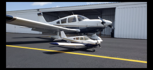 Small blue and white model airplane parked under a larger matching aircraft in a hangar.