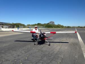 A person kneeling behind a large model airplane on a sunny airstrip.