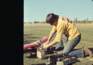 Man kneeling on grass setting up a model airplane.