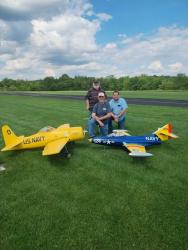 Three people with two large model airplanes on a grassy field.