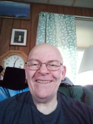 Smiling man with glasses in a cozy room with clock and patterned curtain.