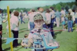 Young boy holding a model helicopter, smiling at an outdoor event.