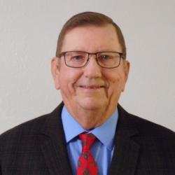 Middle-aged man in a suit, glasses, red tie, smiling.
